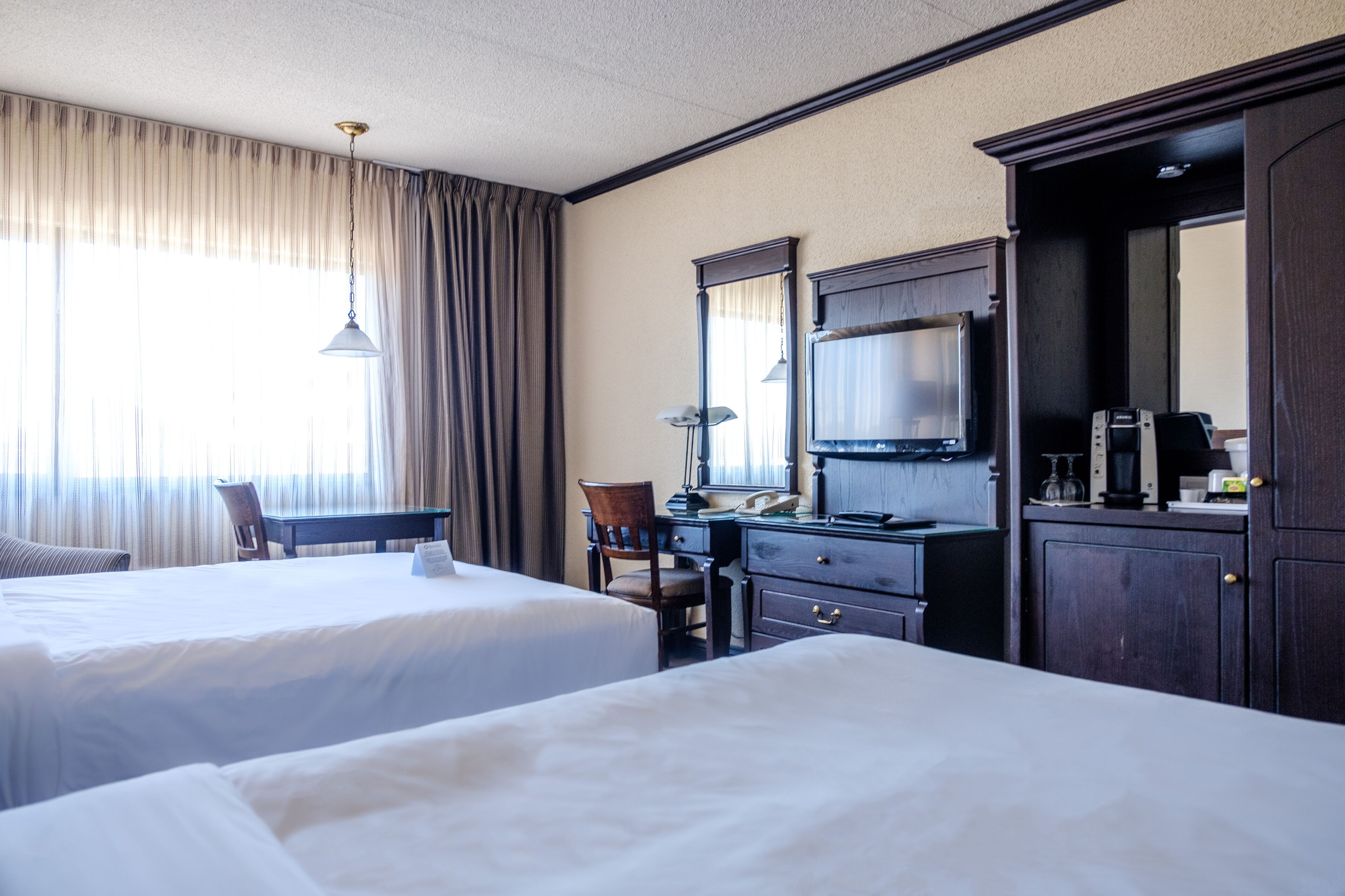 Een hotelkamer met twee bedden, een bureau, een stoel, een dressoir en een grote spiegel.