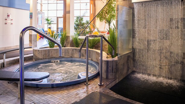A hot tub with a metal railing, surrounded by stone walls and a tiled floor. - Le Montagnais (Saguenay)