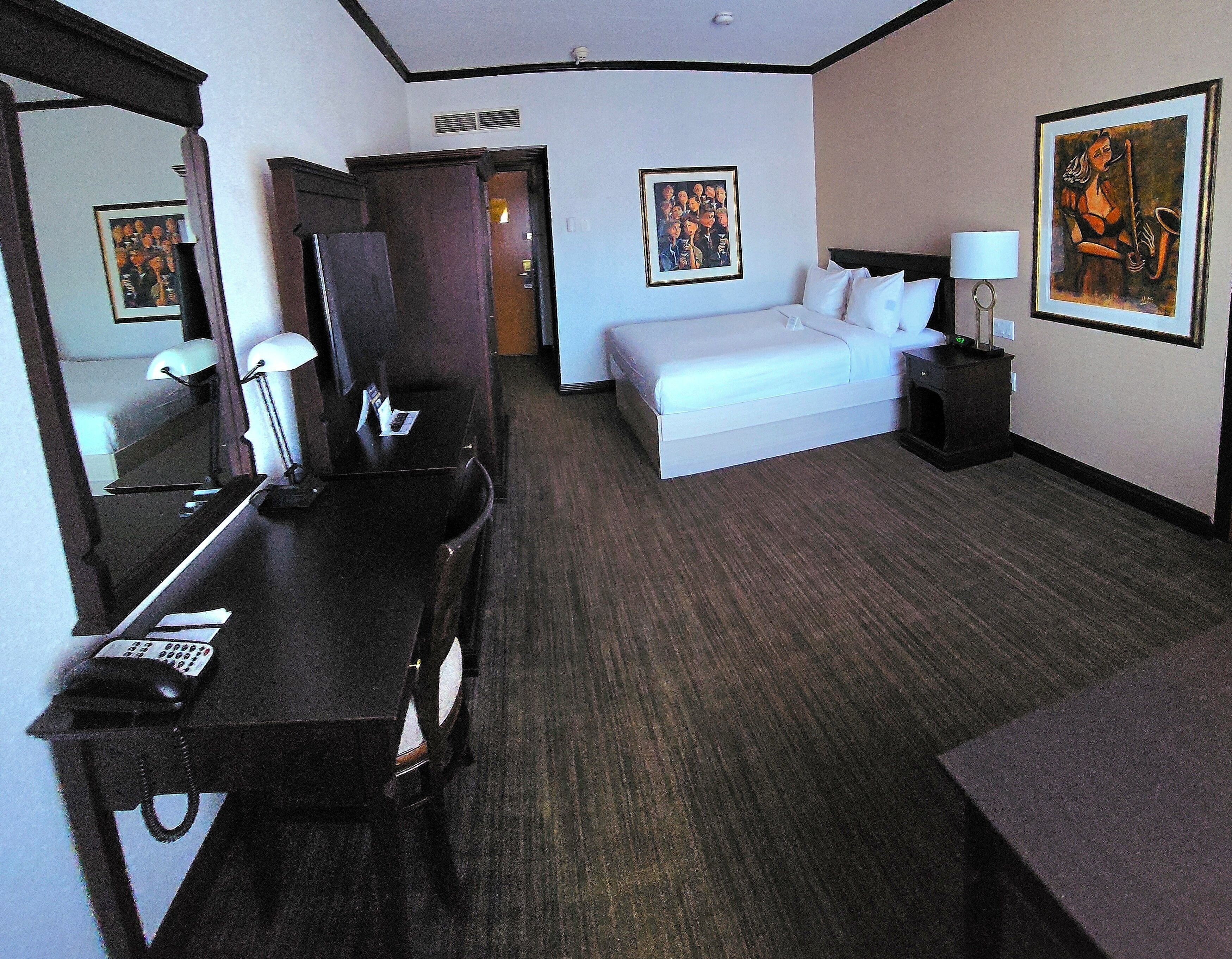 A hotel room with a bed, bedside table, lamp, desk with phone, and a mirror.
