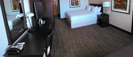 A hotel room with a bed, bedside table, lamp, desk with phone, and a mirror.