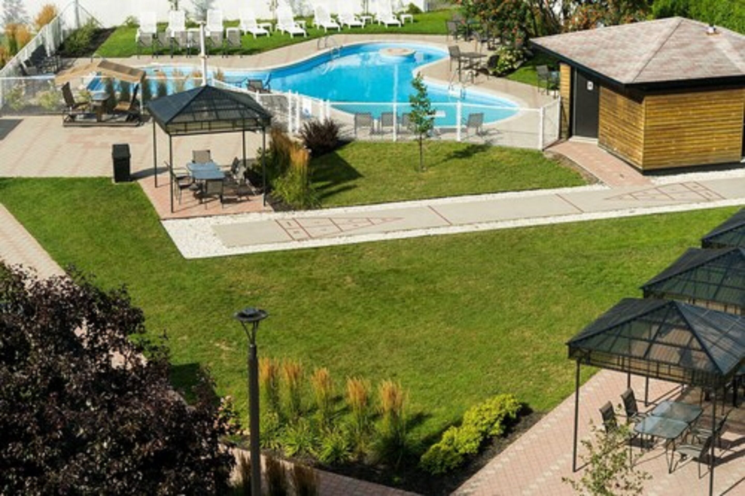 Ein Pool mit Liegestühlen und einem Pavillon, umgeben von gepflegten Rasenflächen und einem kleinen Gebäude.
