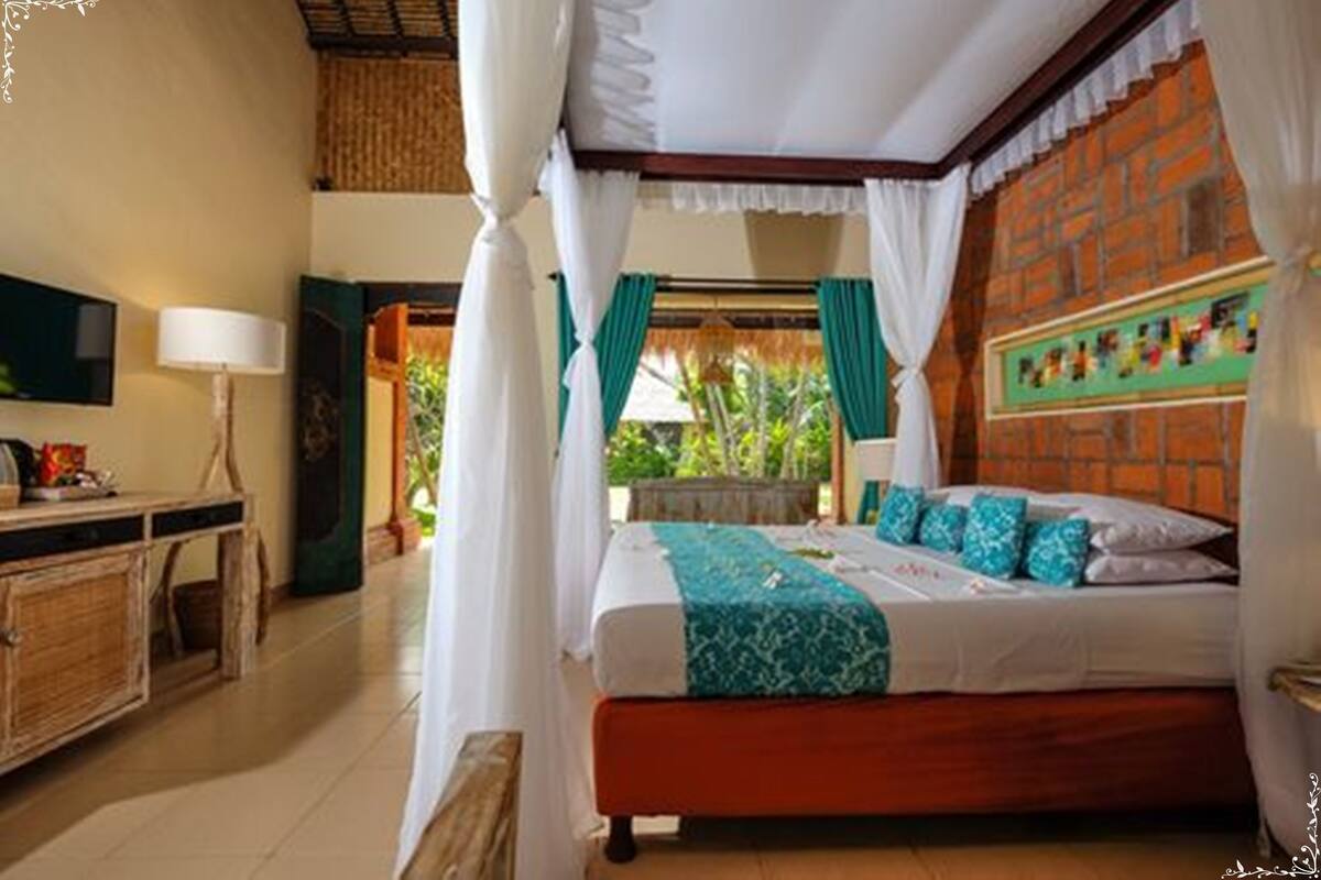 A bedroom with a bed, a TV, a desk, and a window with curtains.