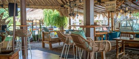 Un restaurante con techo de paja, mobiliario de mimbre y un letrero que dice 'READY to DO NOTHING'.