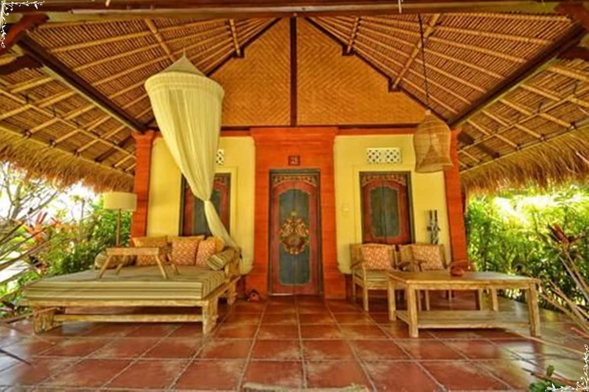 A traditional room with a thatched roof, two beds, a table, and a curtain.