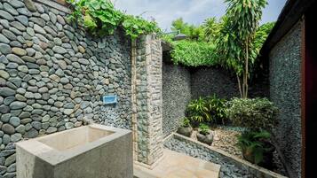 Une salle de bain aux murs en pierre, équipée d’une douche, d’un lavabo et de plantes en pot.