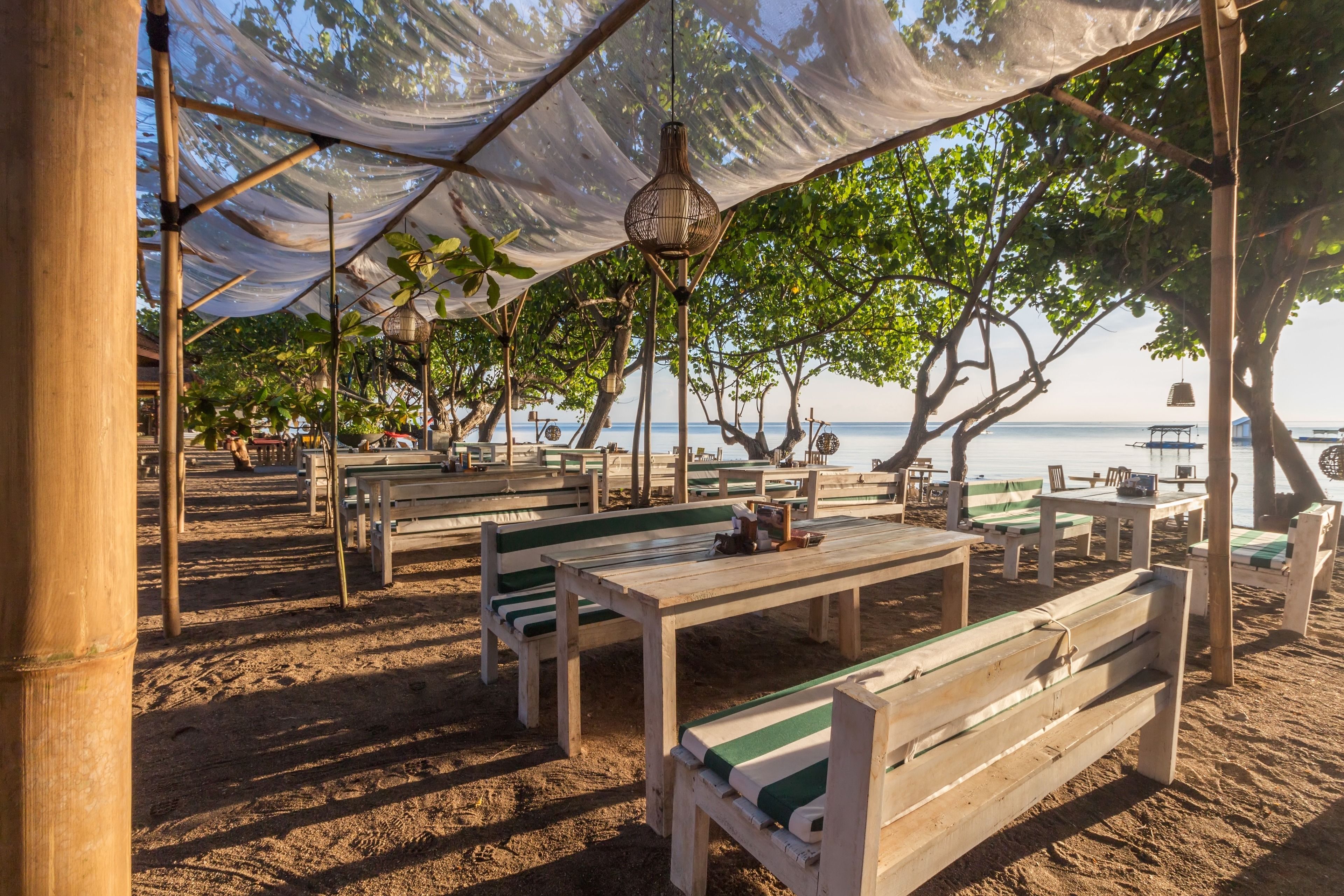 Un café frente al mar con mesas y bancos de madera, cubierto por una marquesina.
