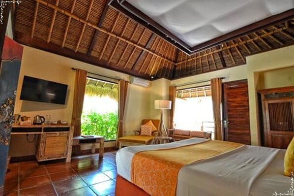 A hotel room with a bed, a desk, a TV, and a window with curtains. - Taman Sari Bali Resort & Spa (Pemuteran)