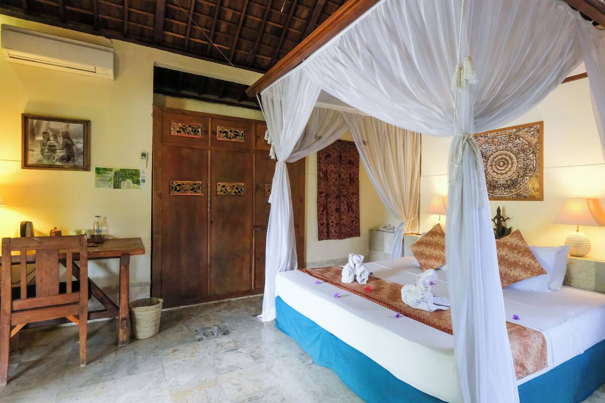 A bedroom with a four-poster bed, a wooden desk, and a chair.
