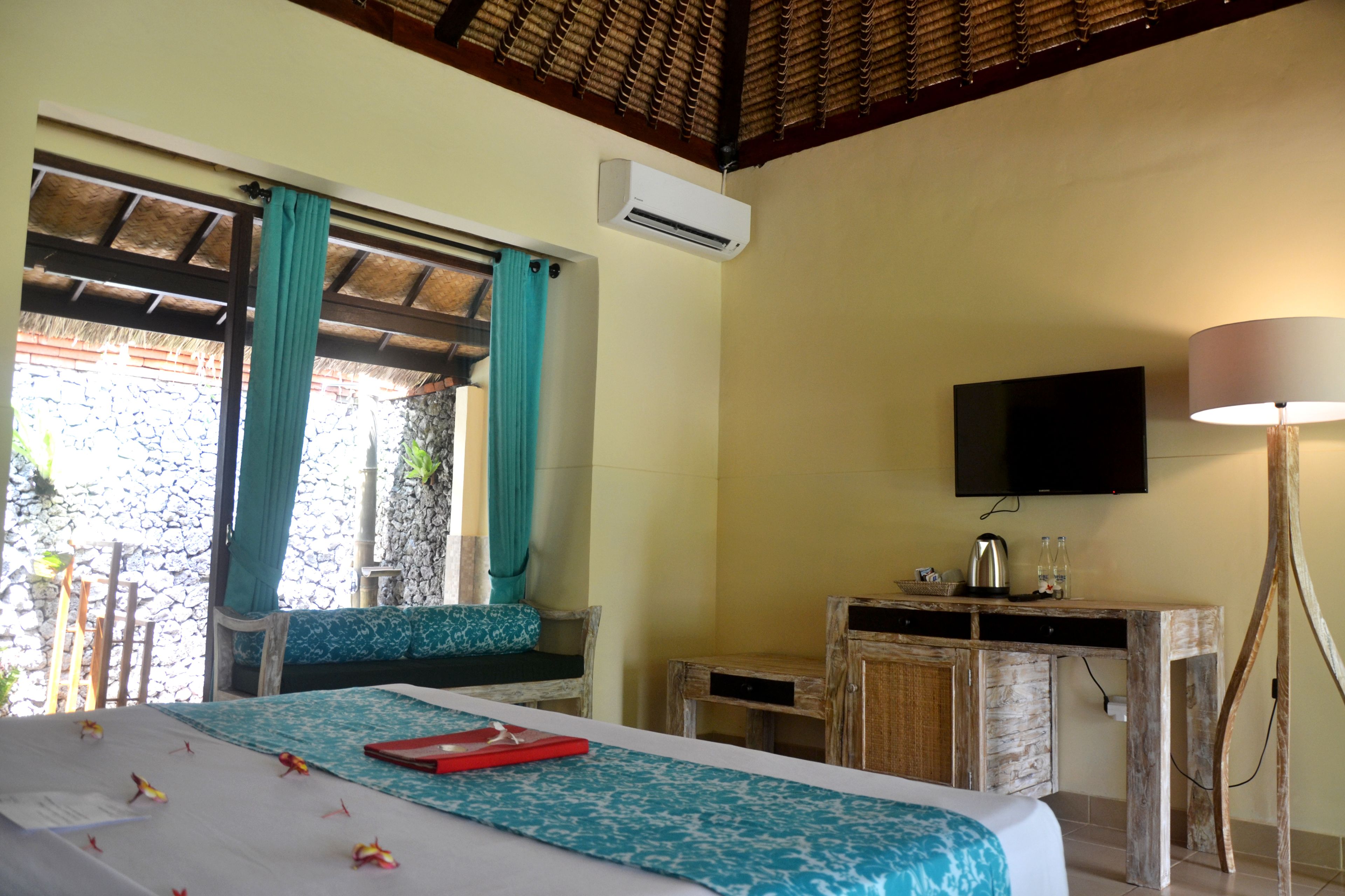 A hotel room with a bed, a desk, a television, and an air conditioning unit.