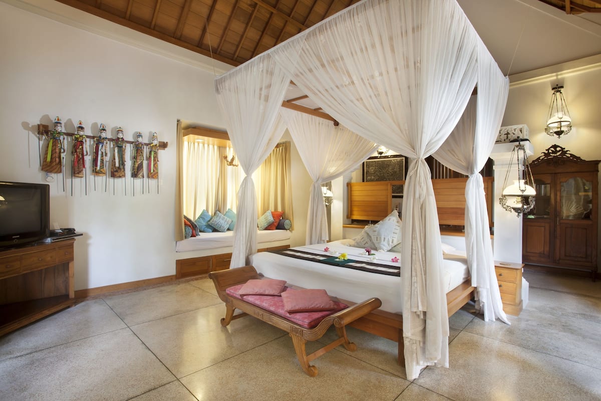 A bedroom with a four-poster bed, a bench with cushions, a television, and a wall with decorative items.