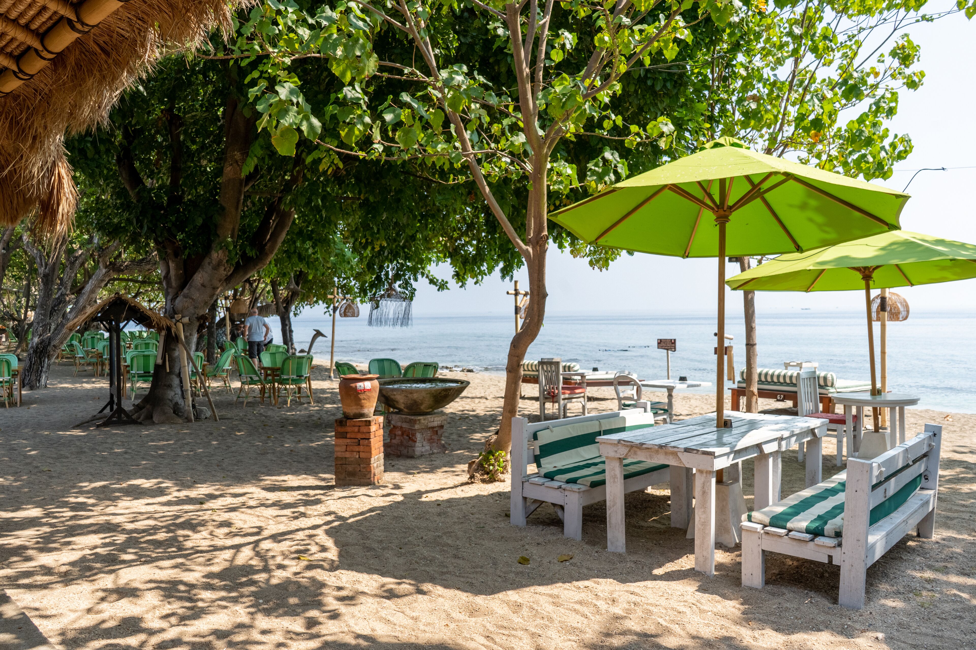 A beachside seating area with tables and chairs, a large umbrella, and a view of the sea.