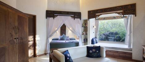 A bedroom with a bed, a sofa, a glass table, and a window with curtains.