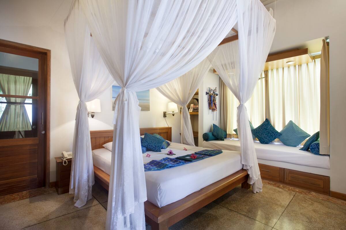 A bedroom with a canopy bed, a bedside table with a lamp, and a window with curtains.