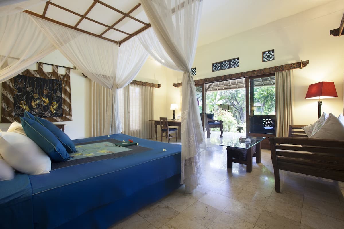 A room with a blue sofa, a wooden bench, a glass coffee table, and a view of greenery outside.