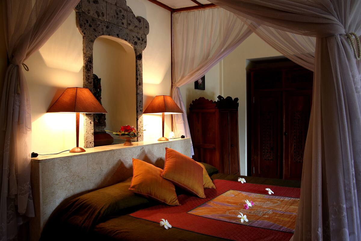 A bedroom with a bed, two lamps, a mirror, and a wooden cabinet.