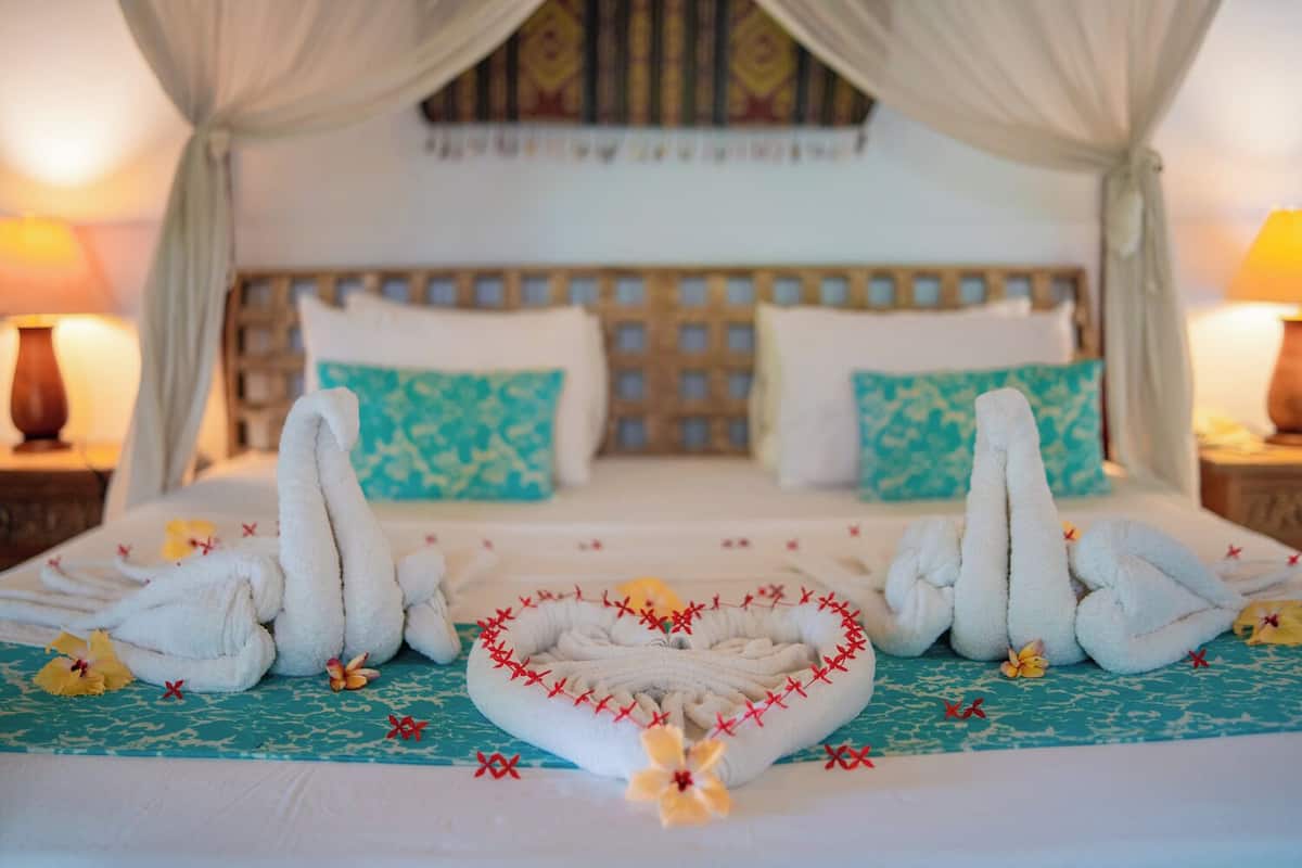 A bed with a canopy, two pillows, and a decorative towel arrangement.