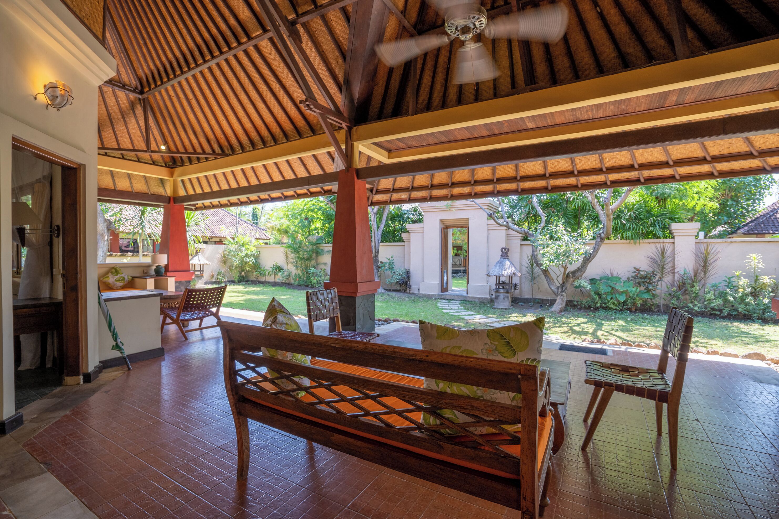 Un patio cubierto con un banco de madera, sillas y un ventilador de techo.