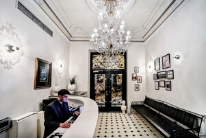 A reception area with a chandelier, black and white patterned floor, a bench, and framed pictures on the wall.
