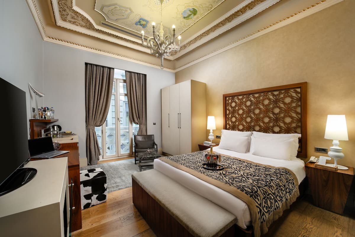 A hotel room with a bed, a desk with a laptop, a chair, a wardrobe, and a chandelier.