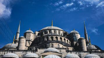 A large, historic building with multiple domes and minarets, likely a mosque, under a clear blue sky.