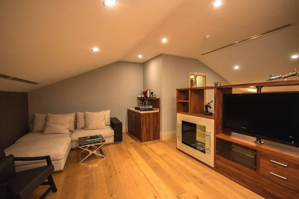 A modern living room with a sofa, TV, wooden entertainment unit, and a fireplace.