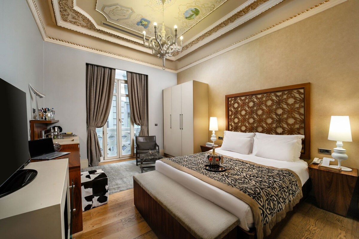 Una habitación de hotel con cama, escritorio, silla, televisor y candelabro.