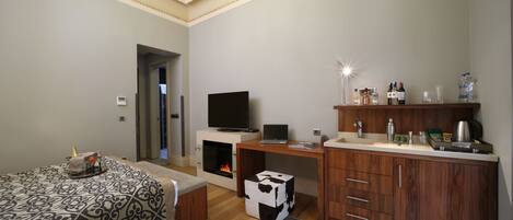 Une chambre d’hôtel moderne équipée d’un lit, d’un bureau avec un ordinateur portable, d’une télévision, d’une cheminée et d’un mini-bar.