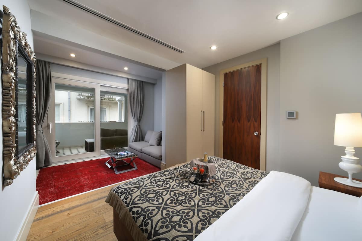 A hotel room with a bed, a nightstand, a red carpet, a sofa, a coffee table, and a large mirror.