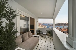 A balcony with a sofa, a chair, and a small table. A potted plant is on the left, and a view of a city and water is visible through the window. - The Story Hotel Pera (Istanbul)