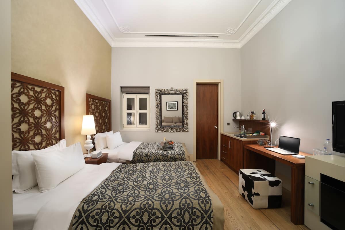 A hotel room with two beds, a desk, a computer, a TV, and a small kitchenette.