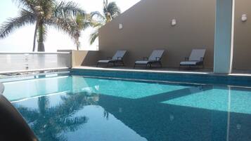 A clear swimming pool with lounge chairs and palm trees in the background.