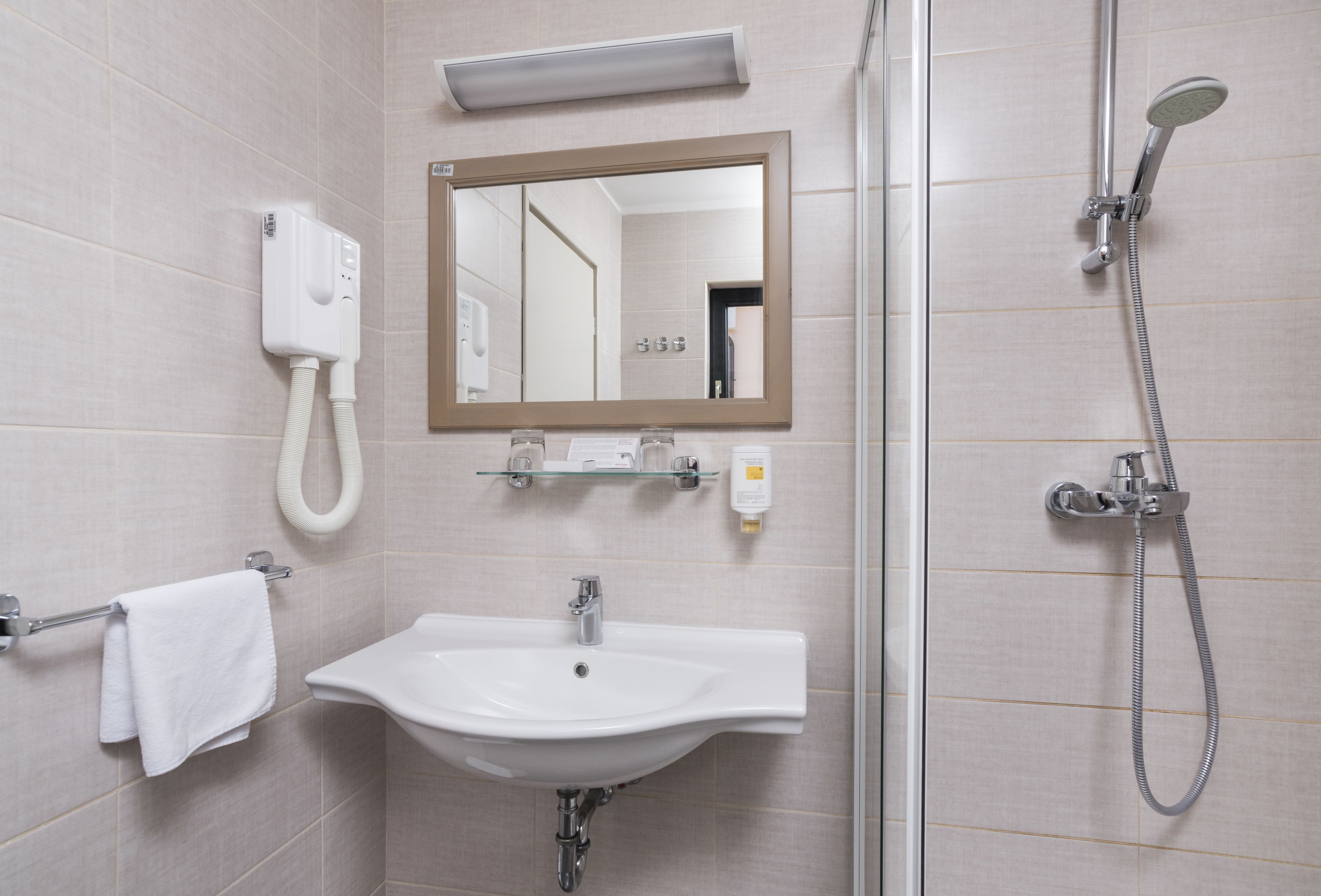 Un baño con un lavamanos blanco, un espejo, un cabezal de ducha manual y un perchero para toallas.