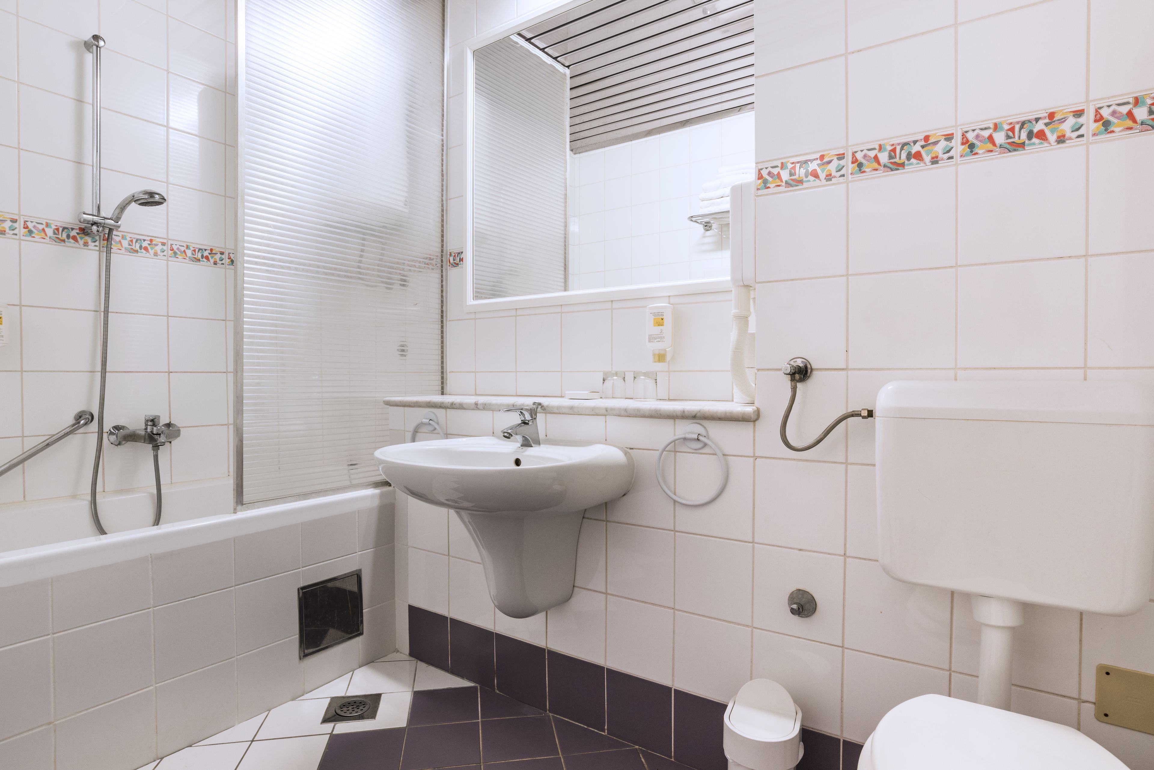 Een badkamer met bad, wastafel, toilet en een raam met zonwering.