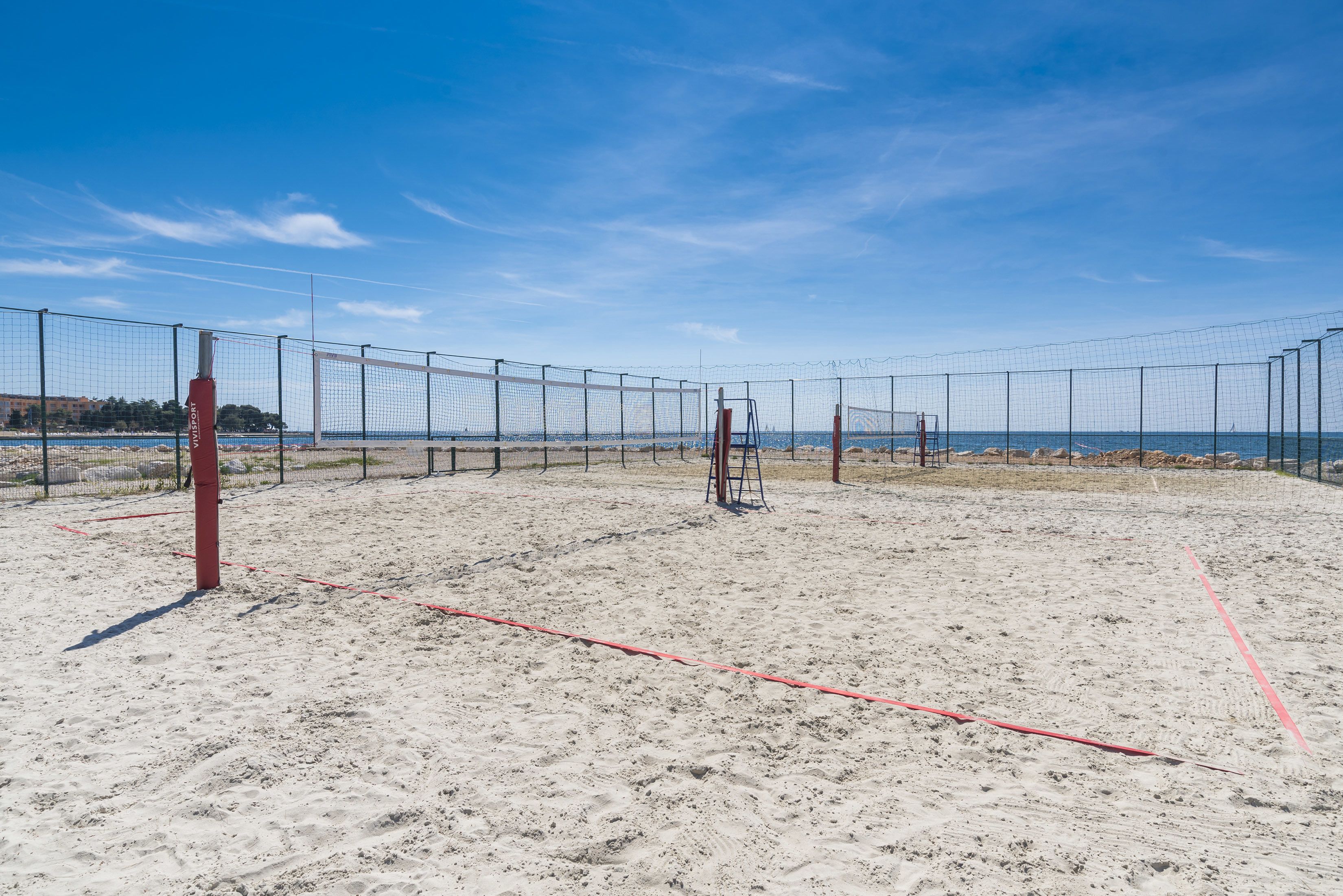 A beach volleyball court with a net, sand, and a clear sky.