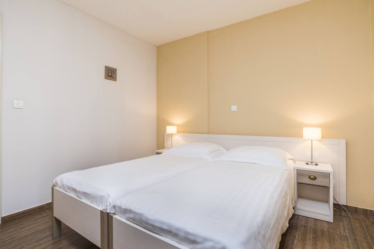 Siististi pedattu sänky valkoisilla lakanoiden kanssa hotellihuoneessa, jossa on puulattia ja beigen sävyiset seinät.