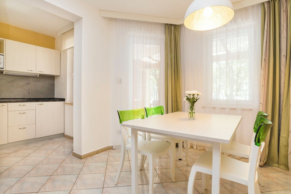 Een moderne keuken met witte kasten, een zwart aanrecht en een witte eettafel met groene stoelen.