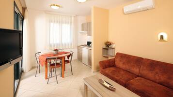 A compact living space with a dining area, a sofa, a TV, and an air conditioning unit.