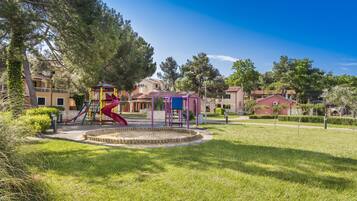 A playground with slides and a climbing structure, surrounded by a well-maintained lawn and trees.