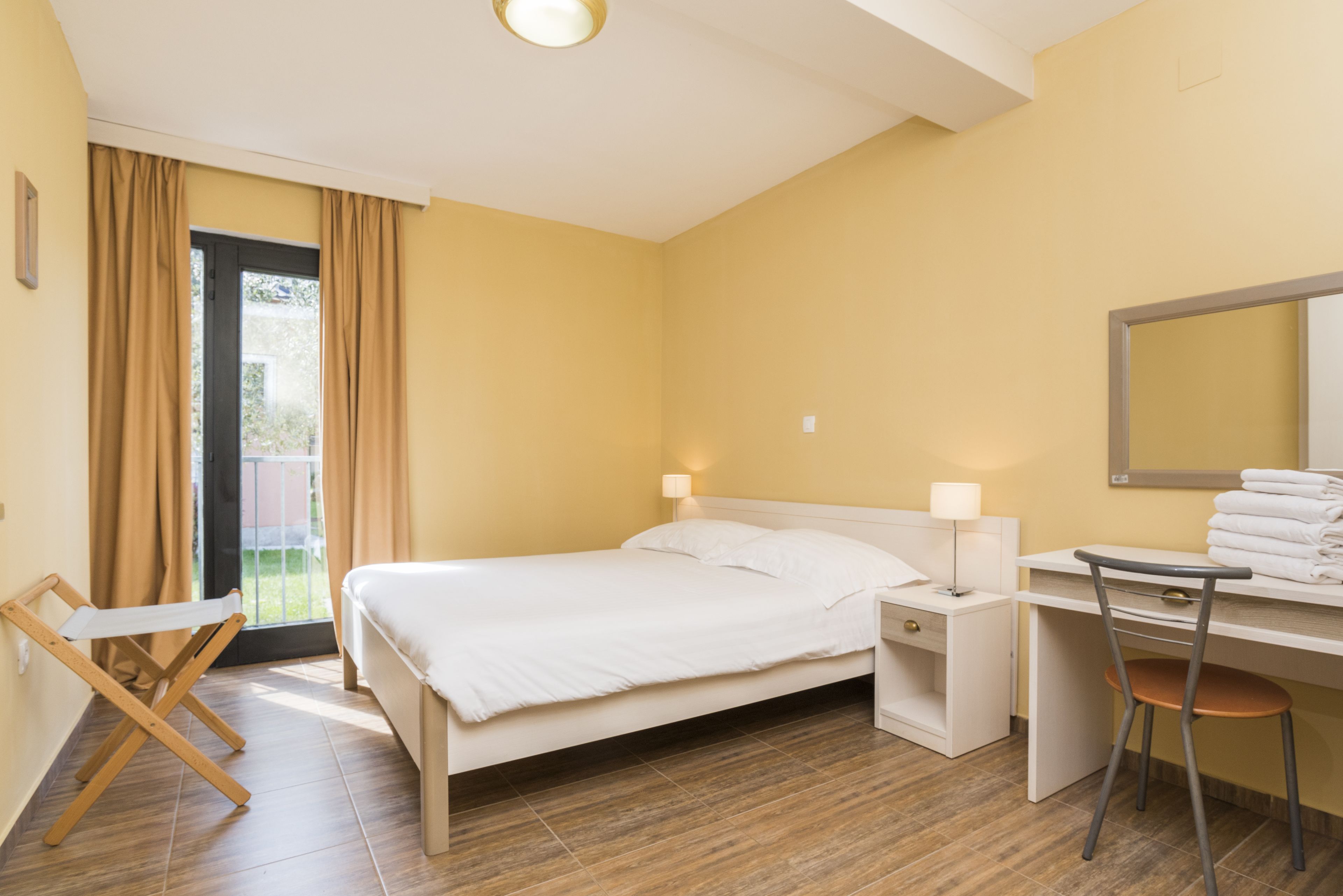 Une chambre à coucher comprenant un lit, une table de chevet, une chaise, un bureau et une fenêtre avec des rideaux.