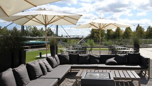 An outdoor seating area with a sofa, two tables, and umbrellas. - Motel One München-Garching (Garching)