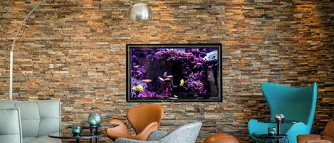 A modern living room with a brick wall, a flat-screen TV, leather and fabric chairs, a round coffee table, and a sports ball.