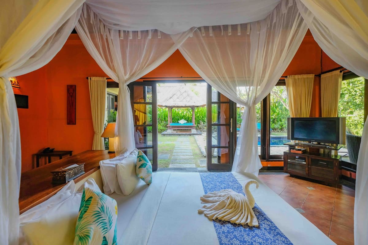 Une chambre à coucher avec un lit, une télévision et une vue sur un jardin, visible à travers une porte vitrée.