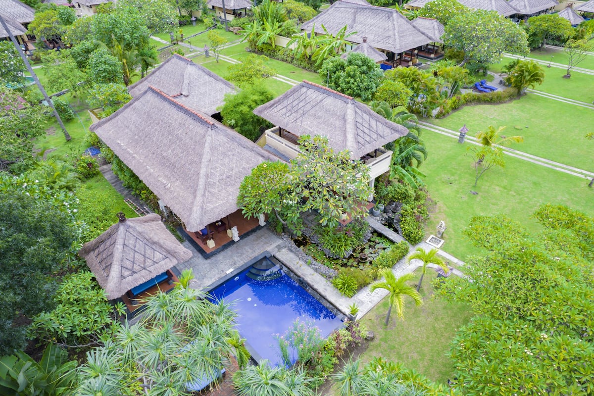 Vue aérienne d’un complexe hôtelier doté de villas aux toits de chaume, d’une piscine centrale et d’une végétation luxuriante.