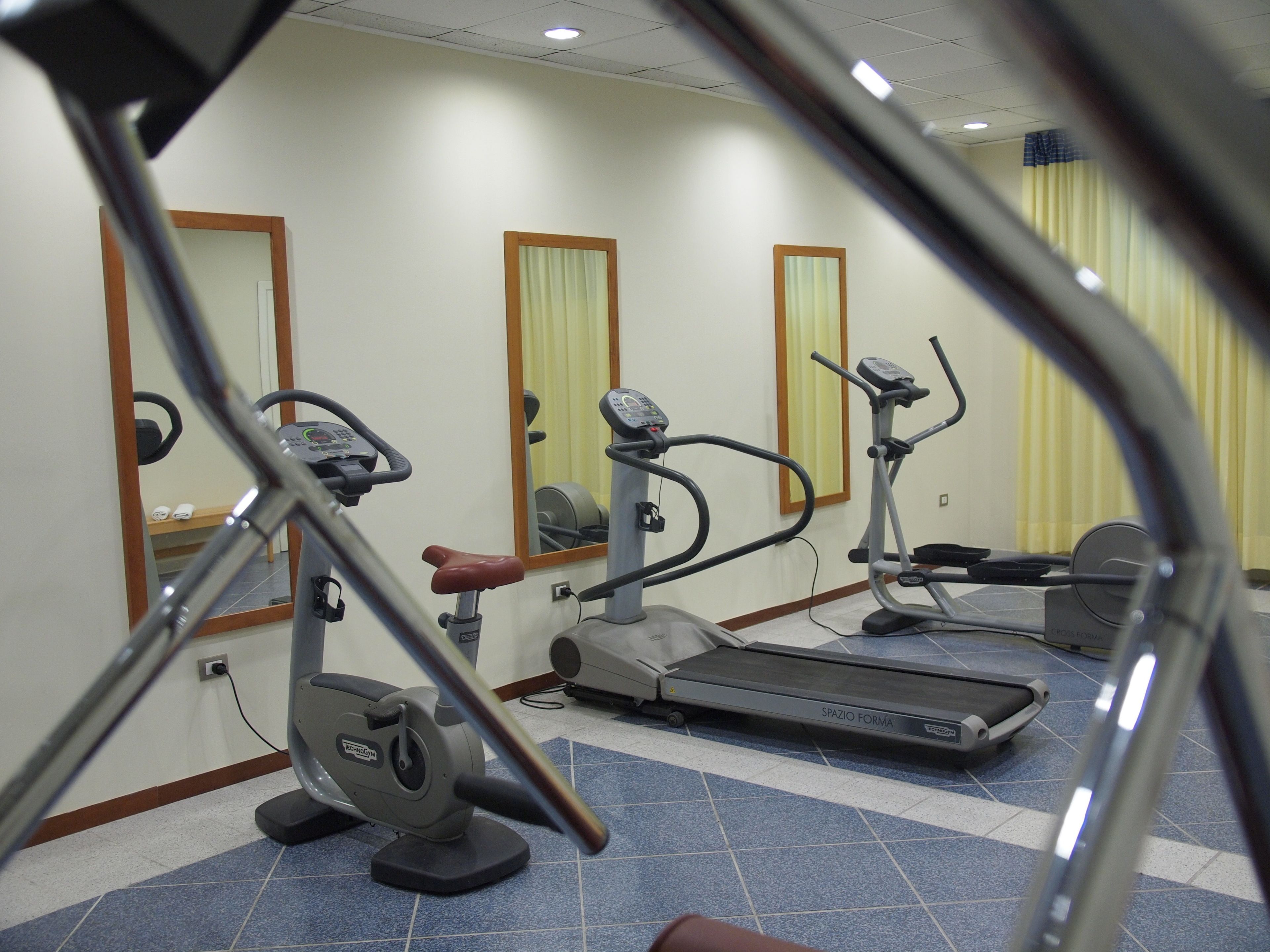 Un gimnasio con máquinas de cardio, incluyendo una cinta de correr y una elíptica, y un espejo en la pared.