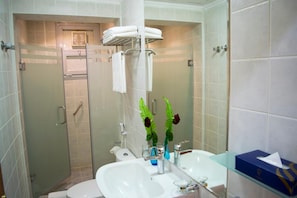 A modern bathroom with a glass shower enclosure, a white sink, and a glass-topped vanity.