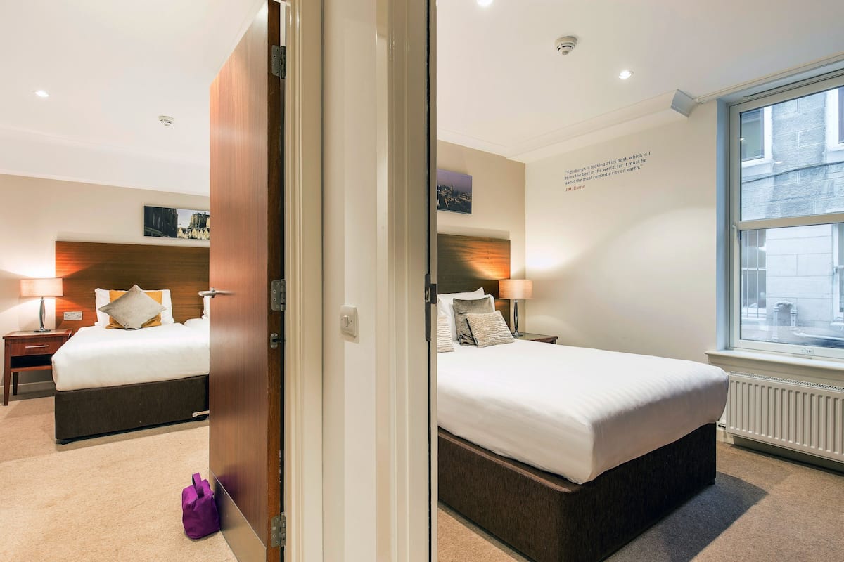A hotel room with two beds, a wooden headboard, a window with a view, and a quote on the wall.