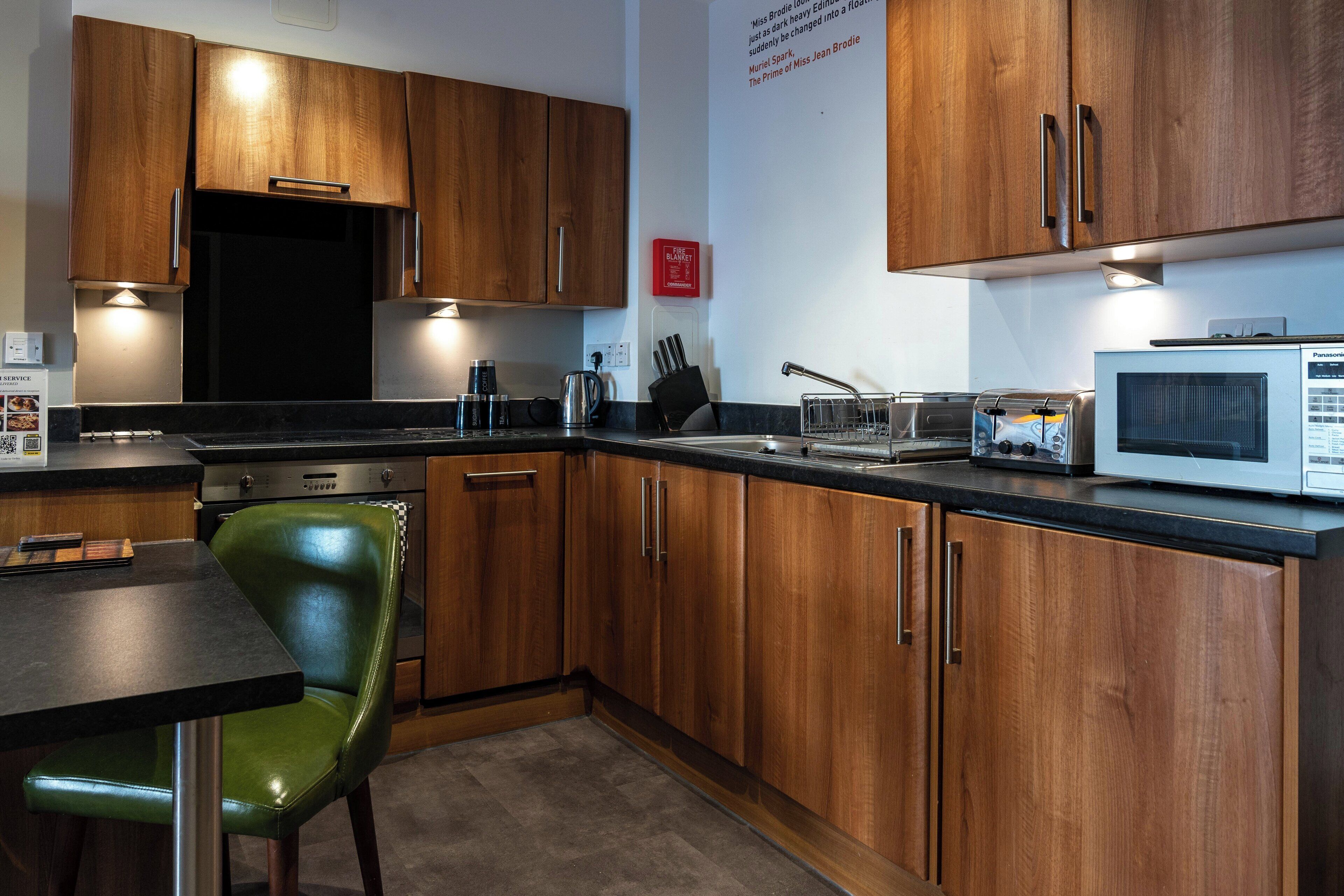 A modern kitchen with wooden cabinets, a stainless steel sink, a microwave, and a green chair.