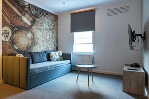 Una habitación con sofá azul, una pequeña mesa redonda, un radiador y una pared con un mapa y una brújula.