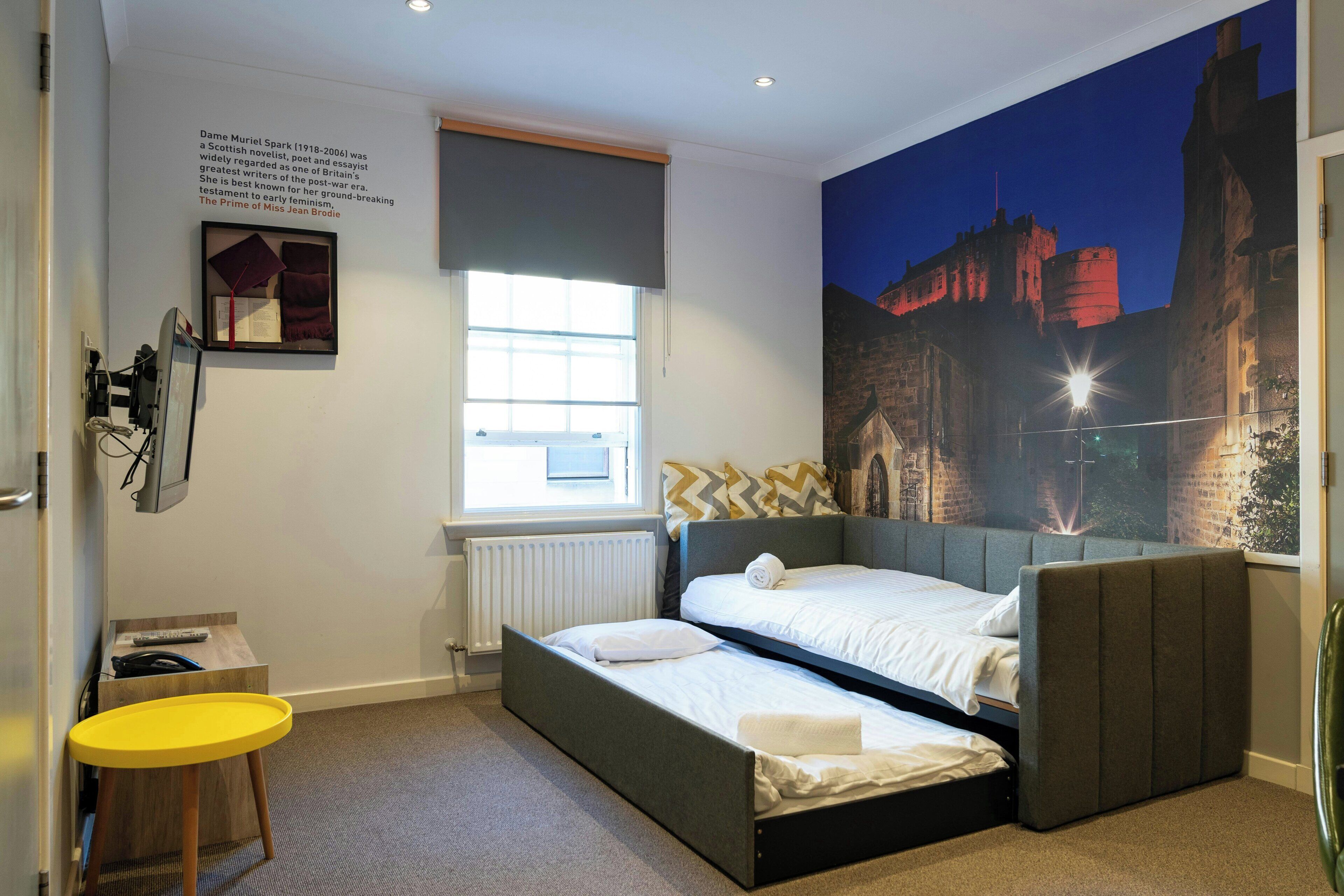 Een slaapkamer met twee bedden, een raam, een radiator, een bureau en een groot muurschilderij.