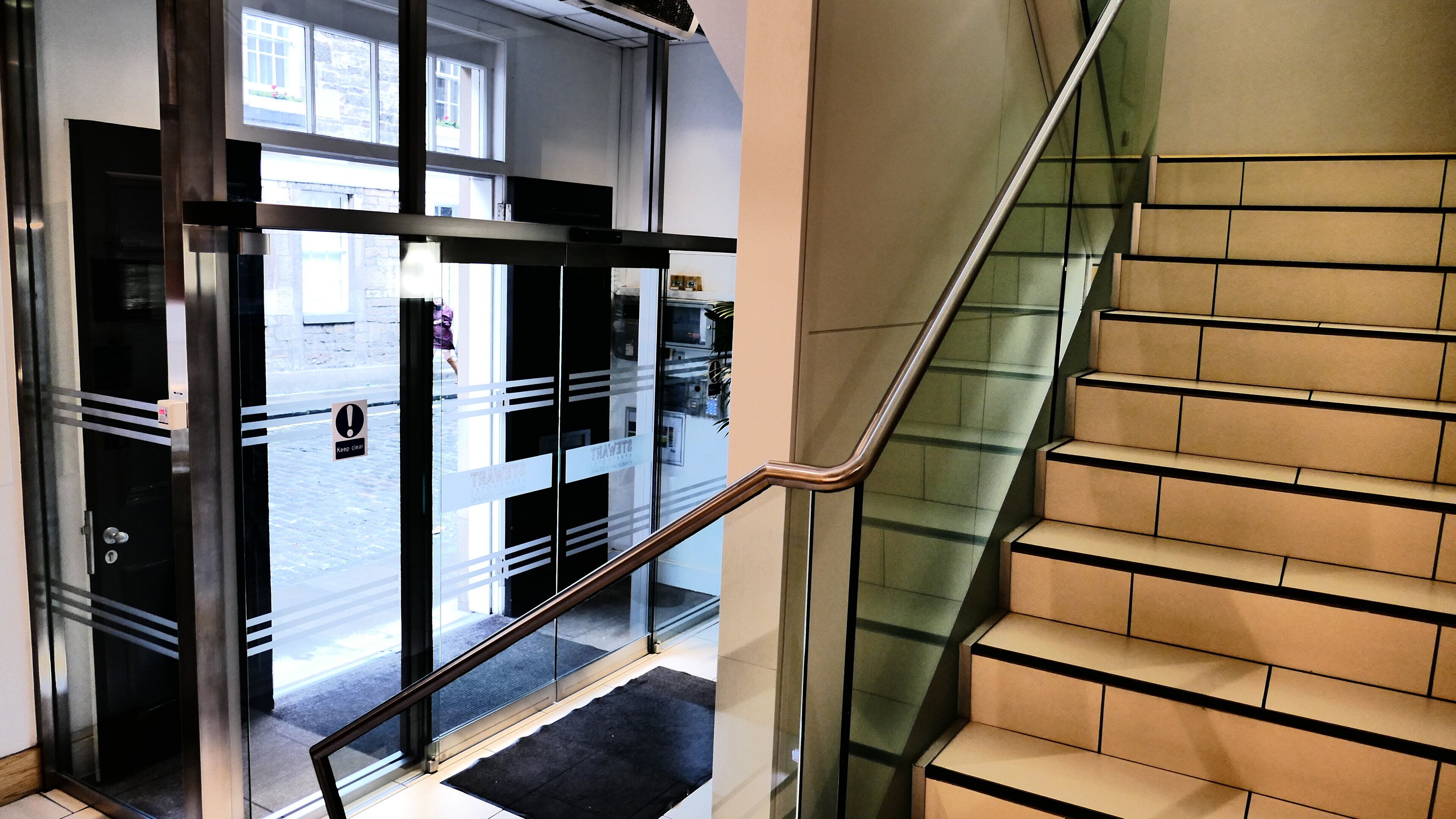 A modern hotel entrance with a glass door, a metal staircase, and a view of the street outside.